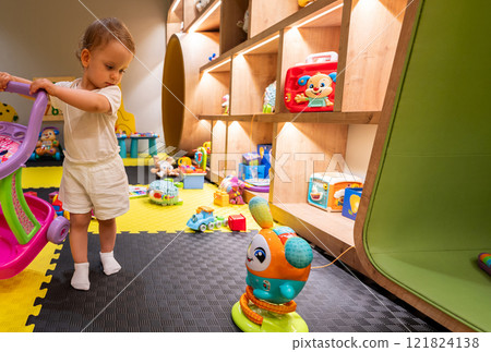 Little child enjoying colorful playroom filled with fun toys. Concept of child-friendly play and learning 121824138