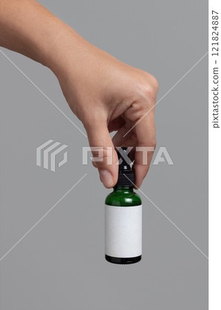 Hand holding dropper bottle with blank label against grey close up, cosmetic mockup Hand holding dropper bottle with blank label against grey close up, cosmetic mockup 121824887