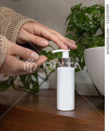 Close up of hands in brown bathrobe pumping liquid on a hand from a cosmetic bottle, mockup 121824894