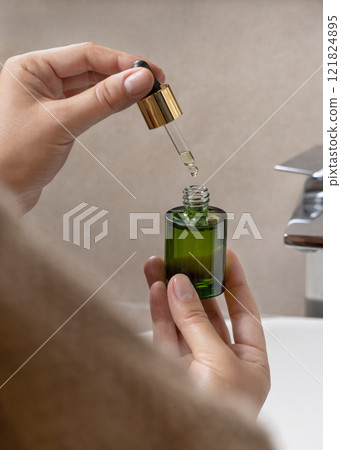 Closeup of woman in brown bathrobe opening green dropper bottle, cosmetic mockup Closeup of woman in brown bathrobe opening green dropper bottle, cosmetic mockup 121824895