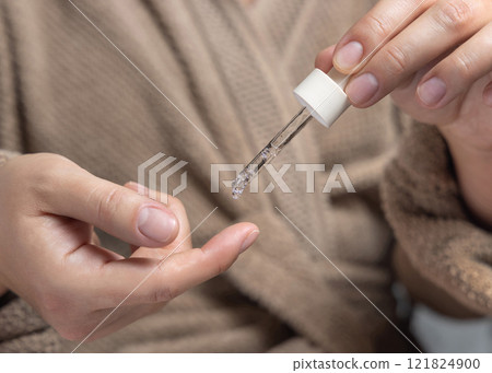 Woman in brown bathrobe dropping essential oil on a finger and holding a pipette closeup Woman in brown bathrobe dropping essential oil on a finger and holding a pipette closeup 121824900