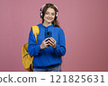 Front view of beautiful schoolgirl standing, taking photo. Young slim brunette female looking at camera, smiling, listening to music in earphones. Concept of modern lifestyle. 121825631
