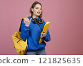 Front view of pretty female with earphones showing rock. Beautiful schoolgirl standing, looking at camera, wearing blue khudi and jeans. Concept of youth and university life. 121825635