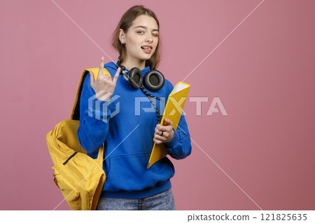Front view of pretty female with earphones showing rock. Beautiful schoolgirl standing, looking at camera, wearing blue khudi and jeans. Concept of youth and university life. Front view of pretty female with earphones showing rock. Beautiful schoolgirl standing, looking at camera, wearing blue khudi and jeans. Concept of youth and university life. 121825635