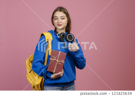Front view of teenage girl standing, holding present, gift box. Beautiful schoolgirl looking at camera, smiling, showing super. Concept of school, college, university and youth. 121825639