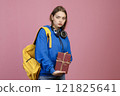 Front view of angry schoolgirl standing, holding bunch of old books. Pretty young student wearing stylish cothes, looking at camera. Concept of education, studying and youth. 121825641