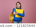 Front view of brunette female brunette standing, holding yellow backpack and rucksack. Pretty schoolgirl wearing blue khudi and jeans, pointing by finger. Concept of youth life. 121825644