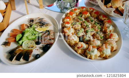 Elegant gourmet canapes displaying shrimp, salmon, red caviar, cucumber on platter, accompanied by smoked fish, lemon, olives Elegant gourmet canapes displaying shrimp, salmon, red caviar, cucumber on platter, accompanied by smoked fish, lemon, olives 121825804