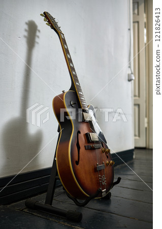 Vintage guitar standing on black floor with shadow on wall in room with open door, musical instrument concept Vintage guitar standing on black floor with shadow on wall in room with open door, musical instrument concept 121826413