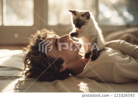 Young man enjoys playful moment with kitten at home during sunny afternoon. Young man enjoys playful moment with kitten at home during sunny afternoon. 121826593