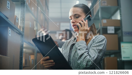 Female Manager Talks with Client on Phone, Uses Tablet Computer in Warehouse 121826606