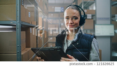 Portrait of Female Logistics Manager Wearing Headset Using Tablet Computer, Looking at Camera 121826625