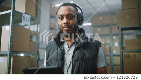 African American Logistics Manager Wearing Headset Uses Tablet Computer, Looks at Camera 121826729