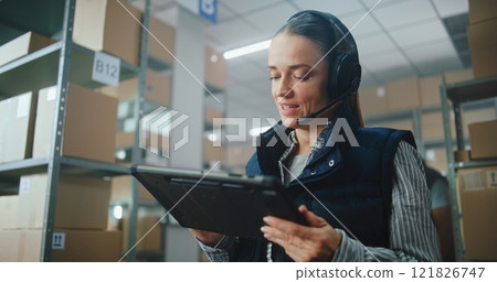 Female Logistics Coordinator Wearing Headset Chats to Customer, Uses Tablet Computer in Warehouse Facility Female Logistics Coordinator Wearing Headset Chats to Customer, Uses Tablet Computer in Warehouse Facility 121826747