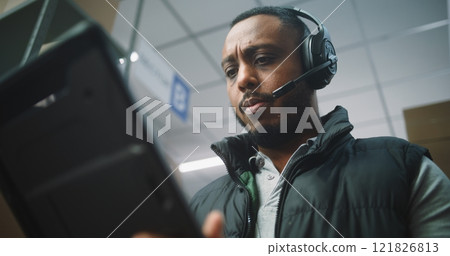 African American Logistics Coordinator Wearing Headset Chats to Customer, Uses Tablet Computer African American Logistics Coordinator Wearing Headset Chats to Customer, Uses Tablet Computer 121826813