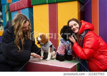 Two women with three dogs enjoying a playful moment in a colorful outdoor setting in winter Two women with three dogs enjoying a playful moment in a colorful outdoor setting in winter 121827563
