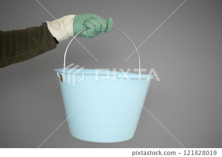 A blue bucket with a handle being held by a gloved hand in a precise manner 121828019