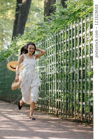 carefree African-American woman in white dress and straw hat runs in park and poses  121828688