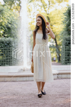 full-length happy African American woman in white dress and straw hat and bag, posing 121828689