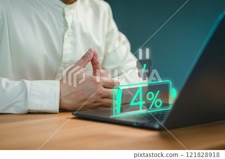 Close-up of a person seated at a desk with a laptop showing a low battery icon at 4%, symbolizing power shortage or urgency. Person appears to be waiting, possibly for the device to charge. 121828918