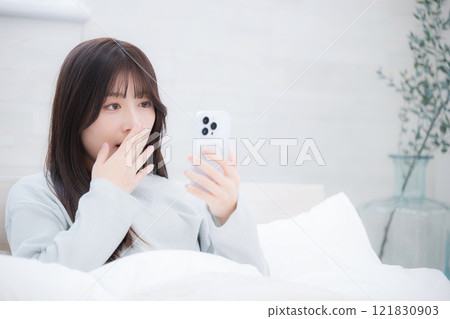 A woman is surprised when she sees a smartphone on her bed 121830903