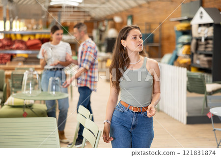 Girl look for something in furniture store, searching for perfect item to complete patio Girl look for something in furniture store, searching for perfect item to complete patio 121831874