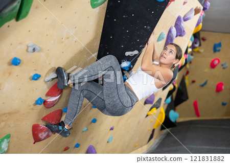 Young woman climbs steep artificial wall in sports complex and trains endurance 121831882