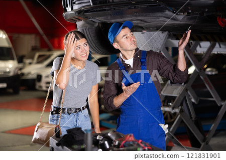 Skilled male auto mechanic controlling automobile detail while young girl looking at it disappointedly 121831901