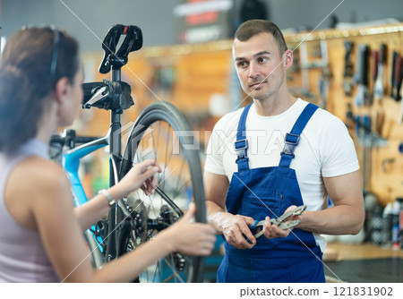 Professional technician examining bike wheel of female client in workshop Professional technician examining bike wheel of female client in workshop 121831902
