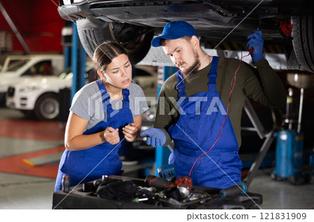 Skilled male auto-mechanic measuring capacity of auto-detail while female worker watching him Skilled male auto-mechanic measuring capacity of auto-detail while female worker watching him 121831909