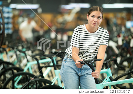 Young woman in bicycle shop choosing new sport bike and selecting model seat Young woman in bicycle shop choosing new sport bike and selecting model seat 121831947