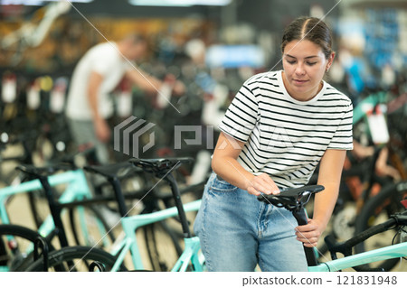 Smiling young girl choosing model seat on high-speed bike in sports shop 121831948