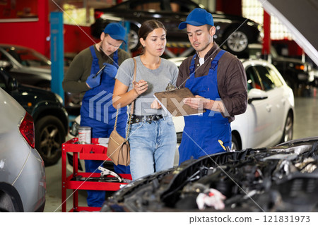 Male worker of auto service speaking to female client concerning his notes on paper 121831973