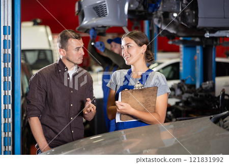 Female worker of auto service speaking to male client concerning her notes on paper Female worker of auto service speaking to male client concerning her notes on paper 121831992