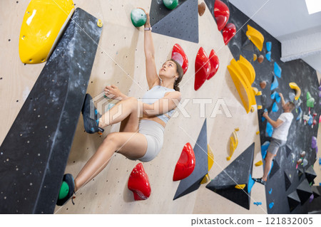 Young woman climbs steep artificial wall in sports complex and trains endurance Young woman climbs steep artificial wall in sports complex and trains endurance 121832005