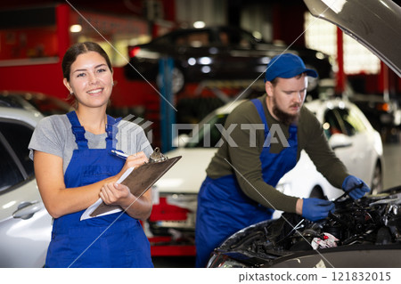 Female car service worker keeps records of work performed by auto mechanics in car service station - makes notes on paper Female car service worker keeps records of work performed by auto mechanics in car service station - makes notes on paper 121832015