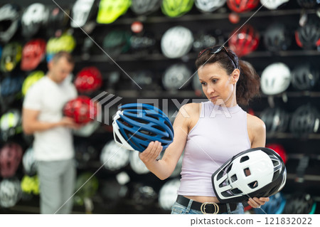 Focused woman comparing bicycle helmets in store of cycling gear Focused woman comparing bicycle helmets in store of cycling gear 121832022