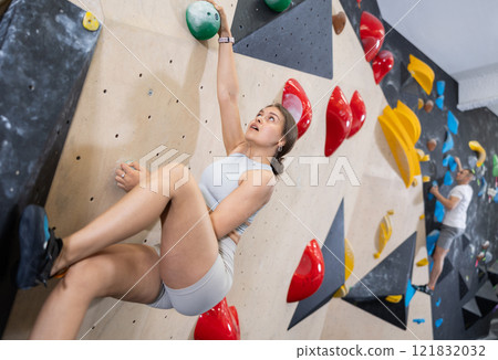 Young woman climbs steep artificial wall in sports complex and trains endurance 121832032