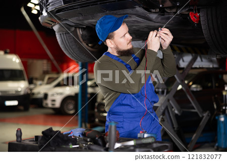 Skilled male auto mechanic in blue overalls measuring capacity of automobile detail 121832077