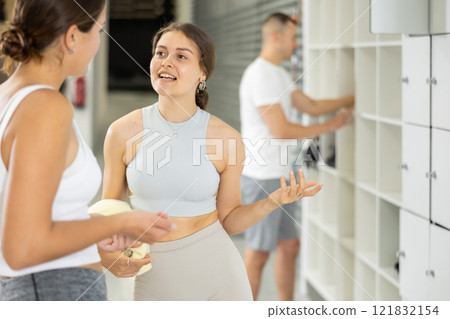 Cheerful girl chatting with female friend by lockers in climbing center Cheerful girl chatting with female friend by lockers in climbing center 121832154