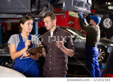Female worker of auto service speaking to male client concerning her notes on paper 121832163