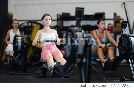 Young woman training at cable row machine with group of sporty people in CrossFit gym Young woman training at cable row machine with group of sporty people in CrossFit gym 121832252