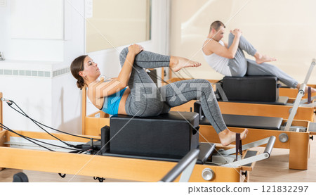Girl doing exercises on reformer using sitting box in pilates studio Girl doing exercises on reformer using sitting box in pilates studio 121832297