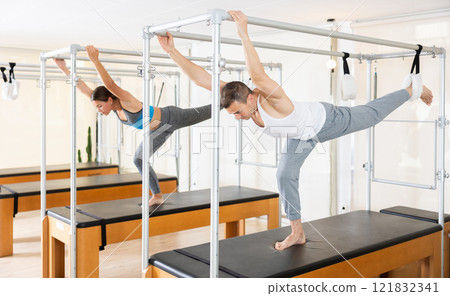 Focused man exercising on trapeze table at group Pilates class 121832341