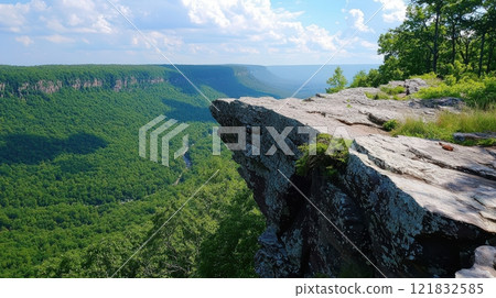 Rocky Outcrop Along Trail Offering Panoramic View of Lush Green Valley and Scenic Mountains Under Blue Sky 121832585
