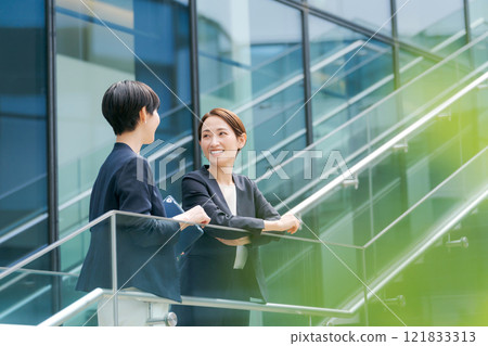 Two businesswomen talking outside a building Two businesswomen talking outside a building 121833313