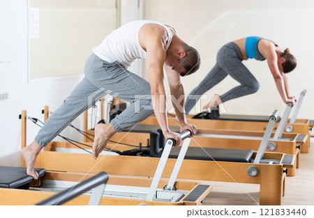 Focused man practicing exercises on Pilates reformer in studio Focused man practicing exercises on Pilates reformer in studio 121833440