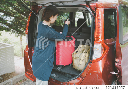 Woman loading suitcases into the trunk of a car 121833657