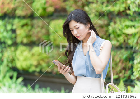 A businesswoman looking at her smartphone in front of a building with green walls 121833662