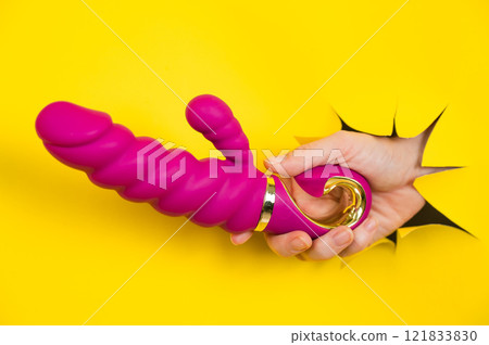 Female hand with magenta vibrator sticking out from yellow paper background. Copy space. 121833830